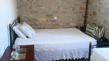 Una camera da letto con parete in pietra, un letto con biancheria bianca, un comodino in legno e un tavolino da notte con una lampada e un piccolo oggetto decorativo.