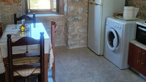 A rustic kitchen with a stone wall, a washing machine, a refrigerator, and a dining table with chairs.
