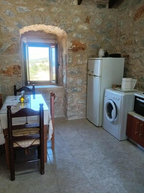 Una cocina rústica con pared de piedra, lavadora, refrigerador y una mesa de comedor con sillas.