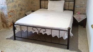 A bedroom with a stone wall, a bed with a metal frame, and a nightstand with a lamp.