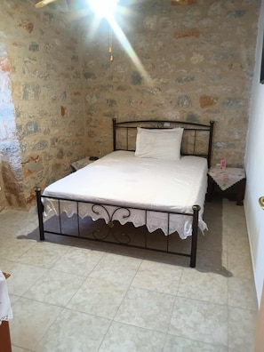 Un dormitorio con pared de piedra, cama con estructura de metal y mesita de noche con lámpara.