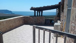 A balcony with a view of the sea, a stone wall, and a metal railing.