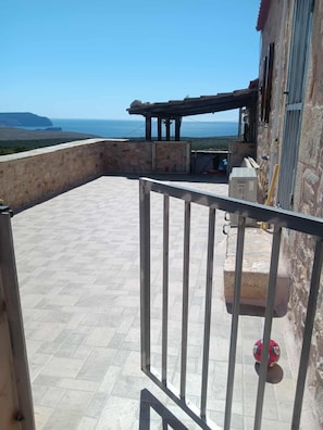 Un balcón con vista al mar, una pared de piedra y una barandilla metálica.