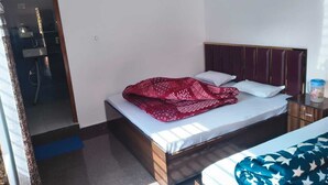Una cama individual con cabecera, una mesita de noche con lámpara, y una ventana que deja entrar luz natural.