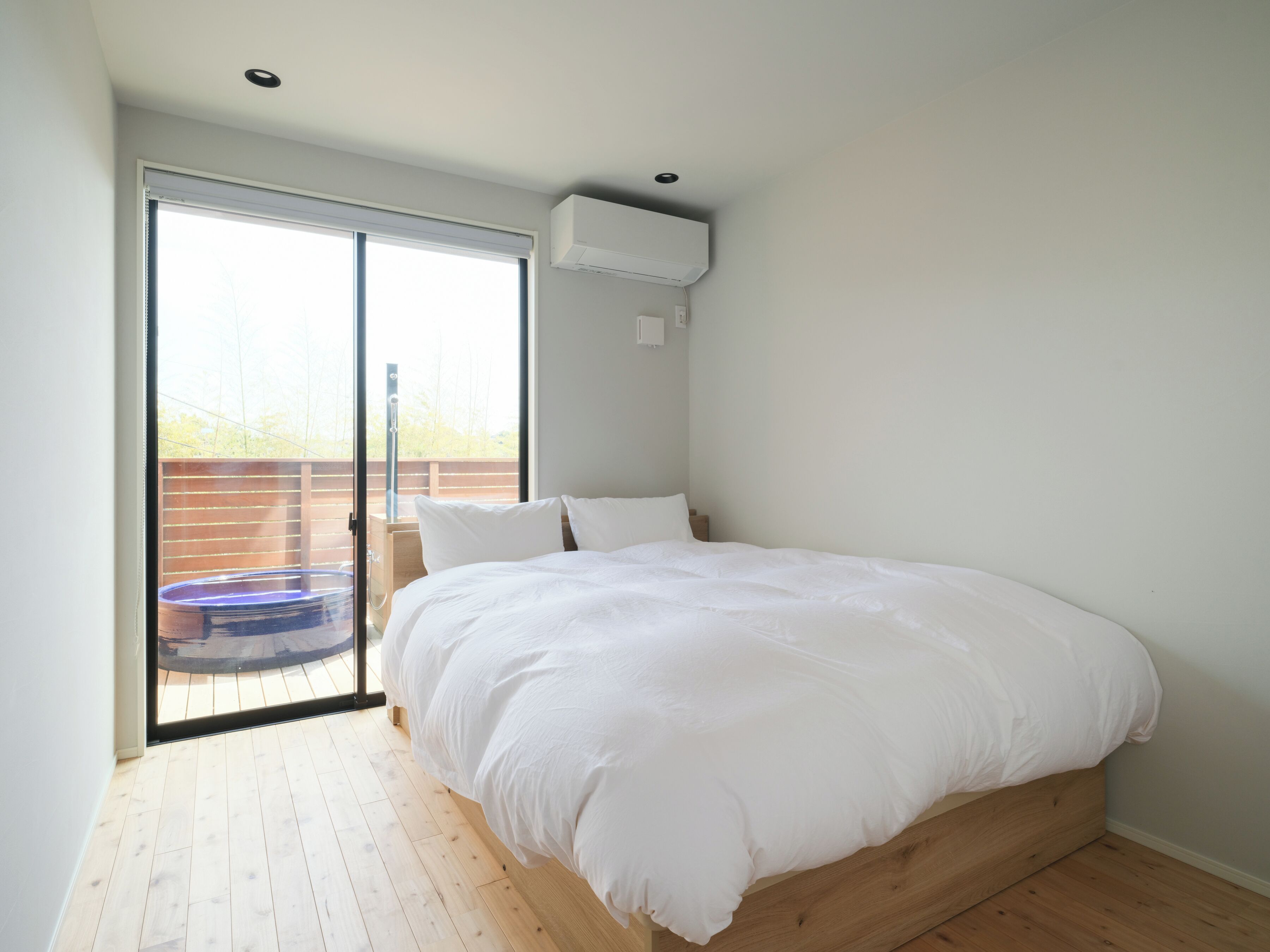 A bedroom with a bed, a sliding glass door to a balcony, and a ceiling-mounted air conditioner.