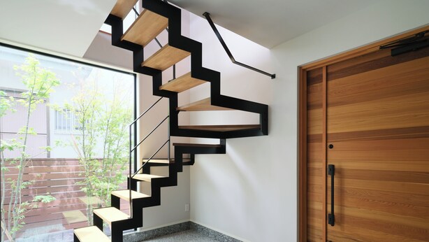 Eine moderne Treppe mit Holzstufen und schwarzen Geländern, die zu einer Tür mit Holzvertäfelung führt.