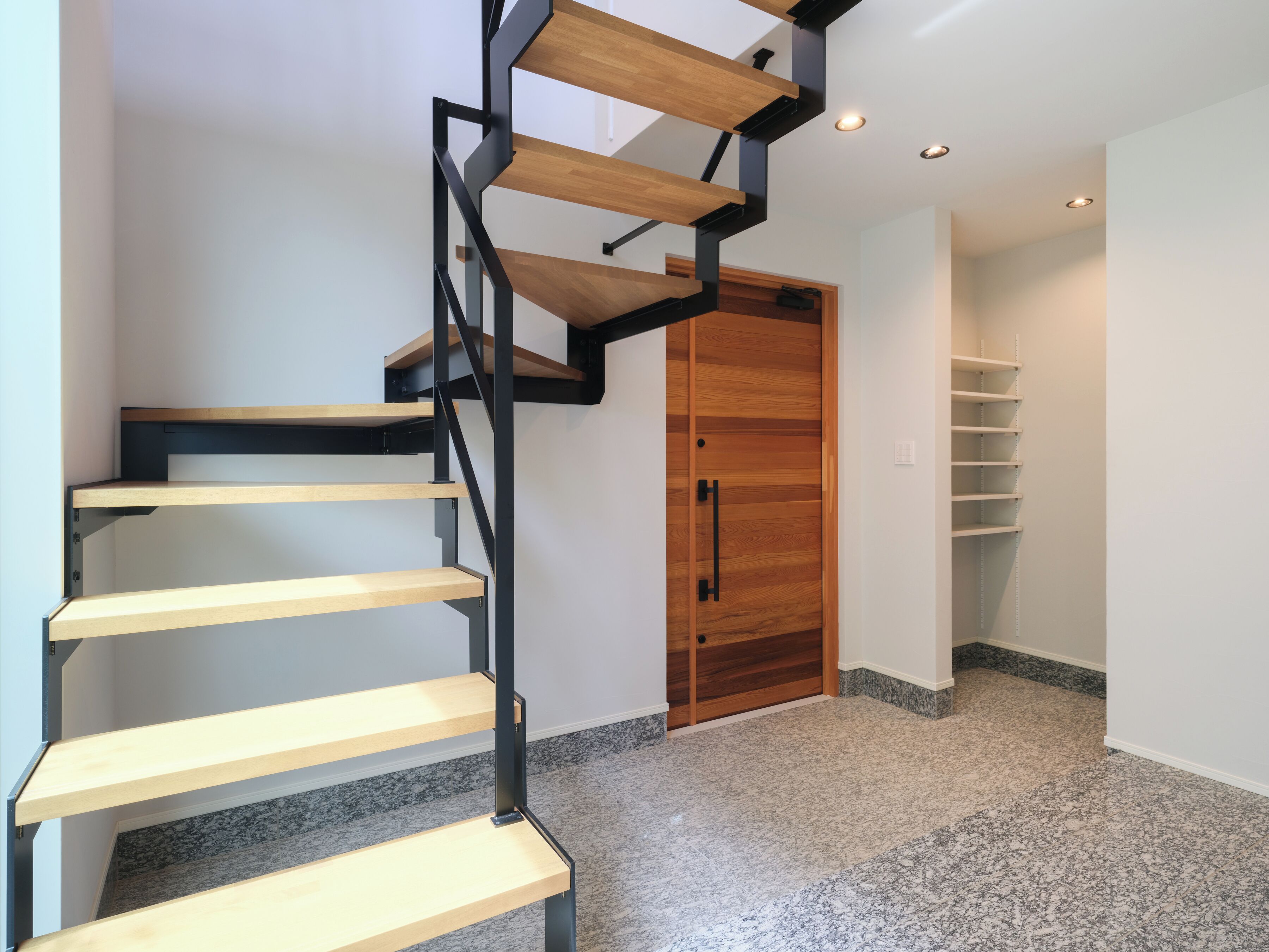 A modern staircase with wooden steps and black metal railings, leading to a wooden door.
