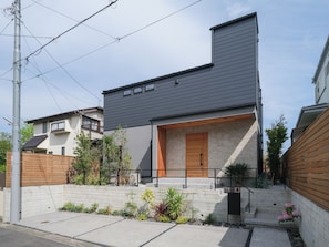 A modern two-story house with a grey roof, a wooden front door, and a small front yard with plants. - KAMAKURA VILLA SAUNA KOSHIGOE 5 (Koshigoe, Kamakura-shi)