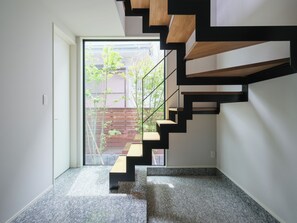 Eine moderne Treppe mit Holzboden und schwarzen Geländern, die zu einer Tür mit Blick auf Grünanlagen führt.