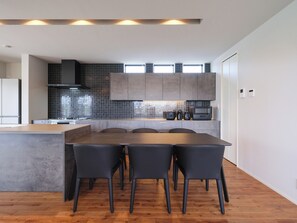 A modern kitchen with a central island, dark chairs, and a wooden floor. - KAMAKURA VILLA SAUNA KOSHIGOE 5 (Koshigoe, Kamakura-shi)