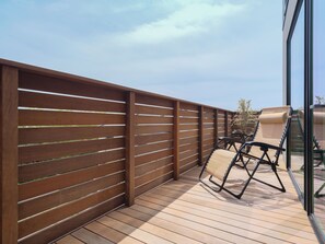A wooden deck with a glass railing, a beige cushioned chair, and a clear sky. - KAMAKURA VILLA SAUNA KOSHIGOE 5 (Koshigoe, Kamakura-shi)