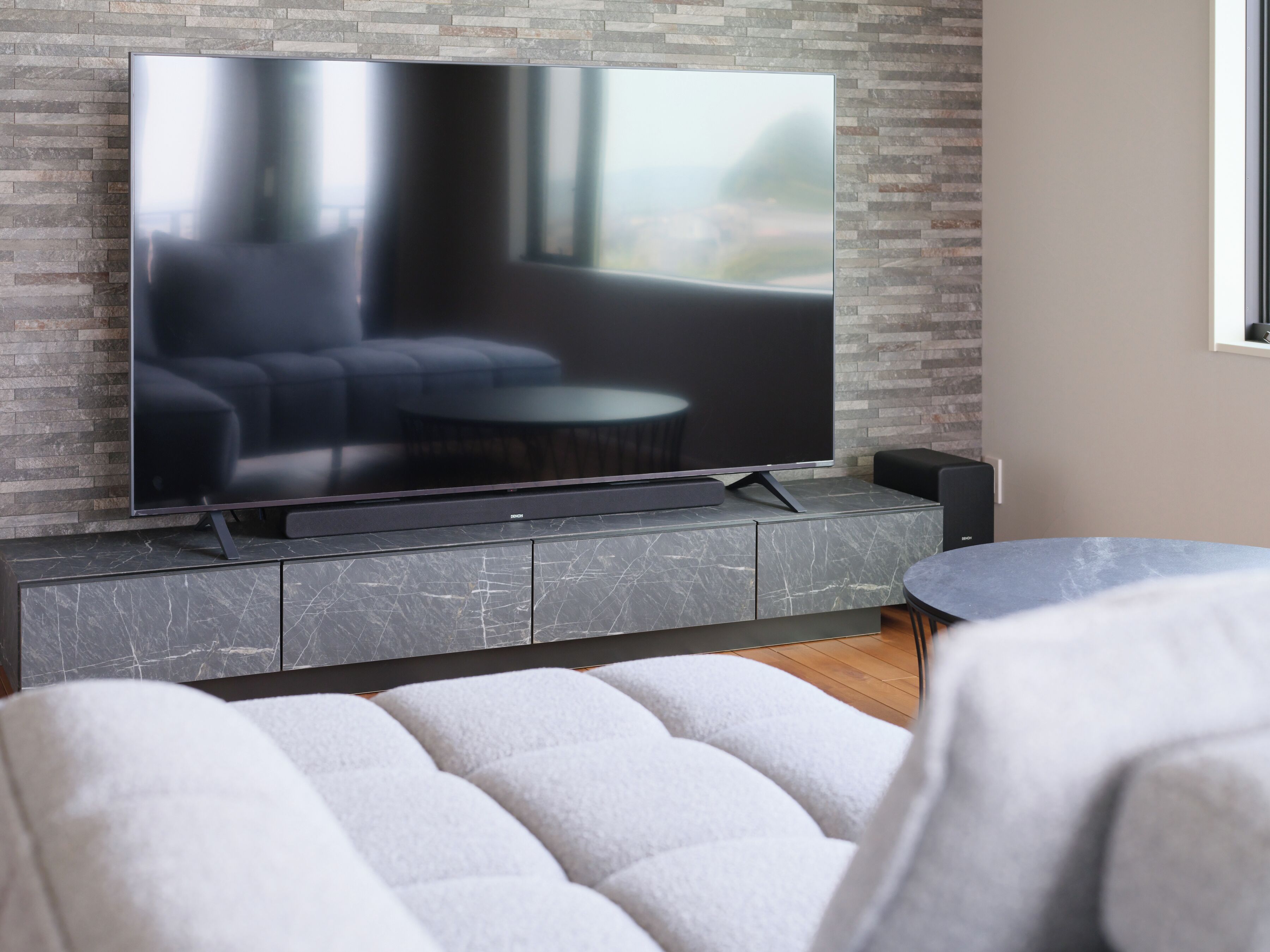 A modern living room with a flat-screen TV on a marble console, a grey sofa, and a round coffee table.