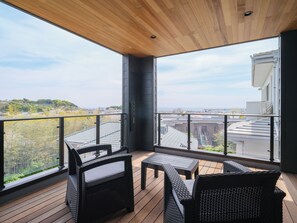A balcony with wicker furniture, a wooden ceiling, and a view of buildings and greenery. - KAMAKURA VILLA SAUNA KOSHIGOE 5 (Koshigoe, Kamakura-shi)