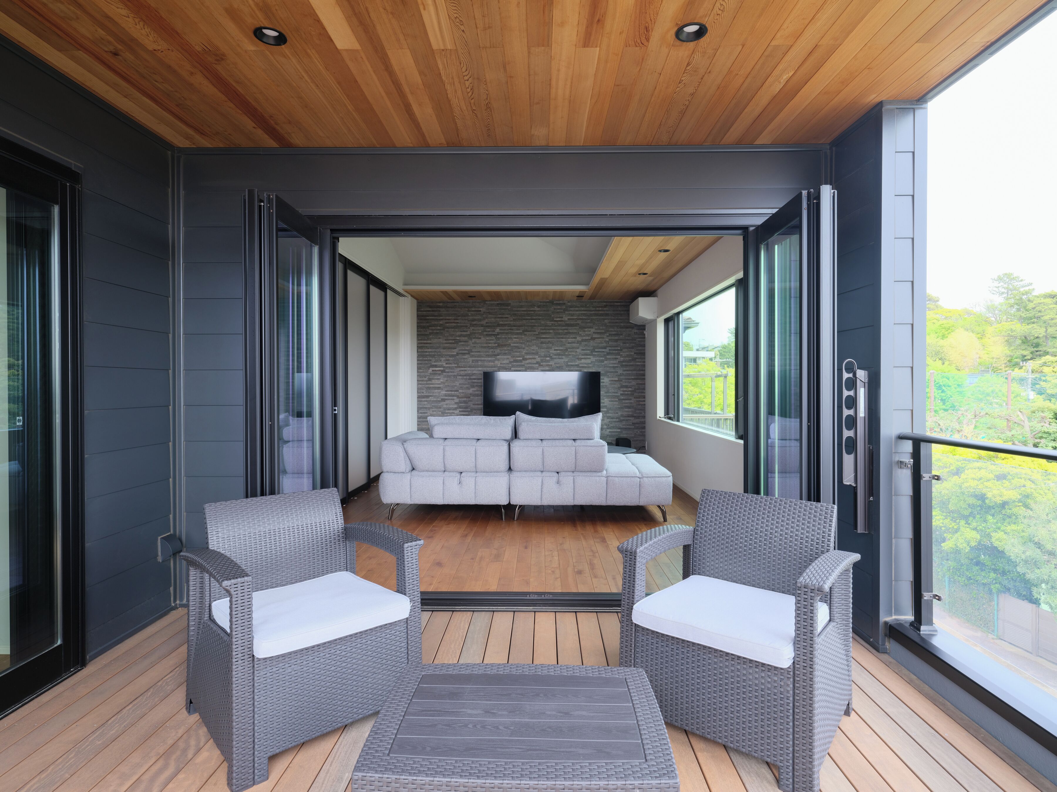 Un intérieur moderne avec un canapé, deux fauteuils, un téléviseur et un balcon doté d’une terrasse en bois.