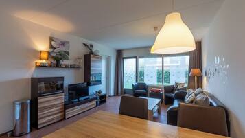 Een moderne woonkamer met een eettafel, banken, een televisie en een groot raam.