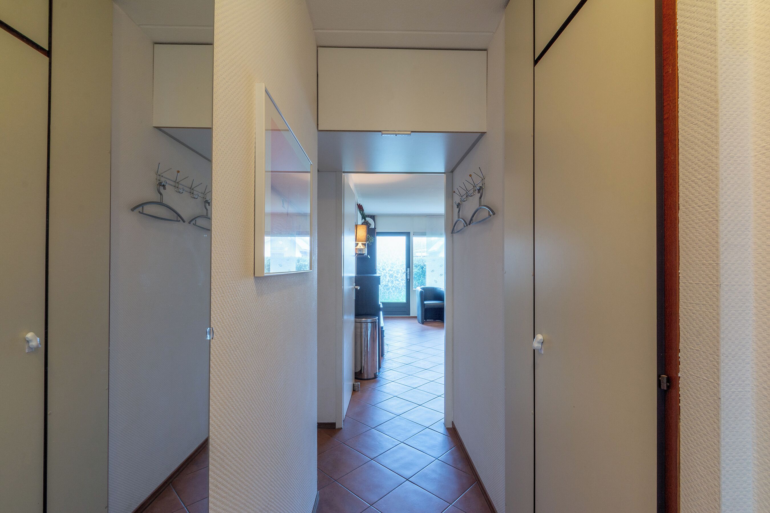 Een gang met zicht op een balkon, een prullenbak en een deur aan de rechterkant.