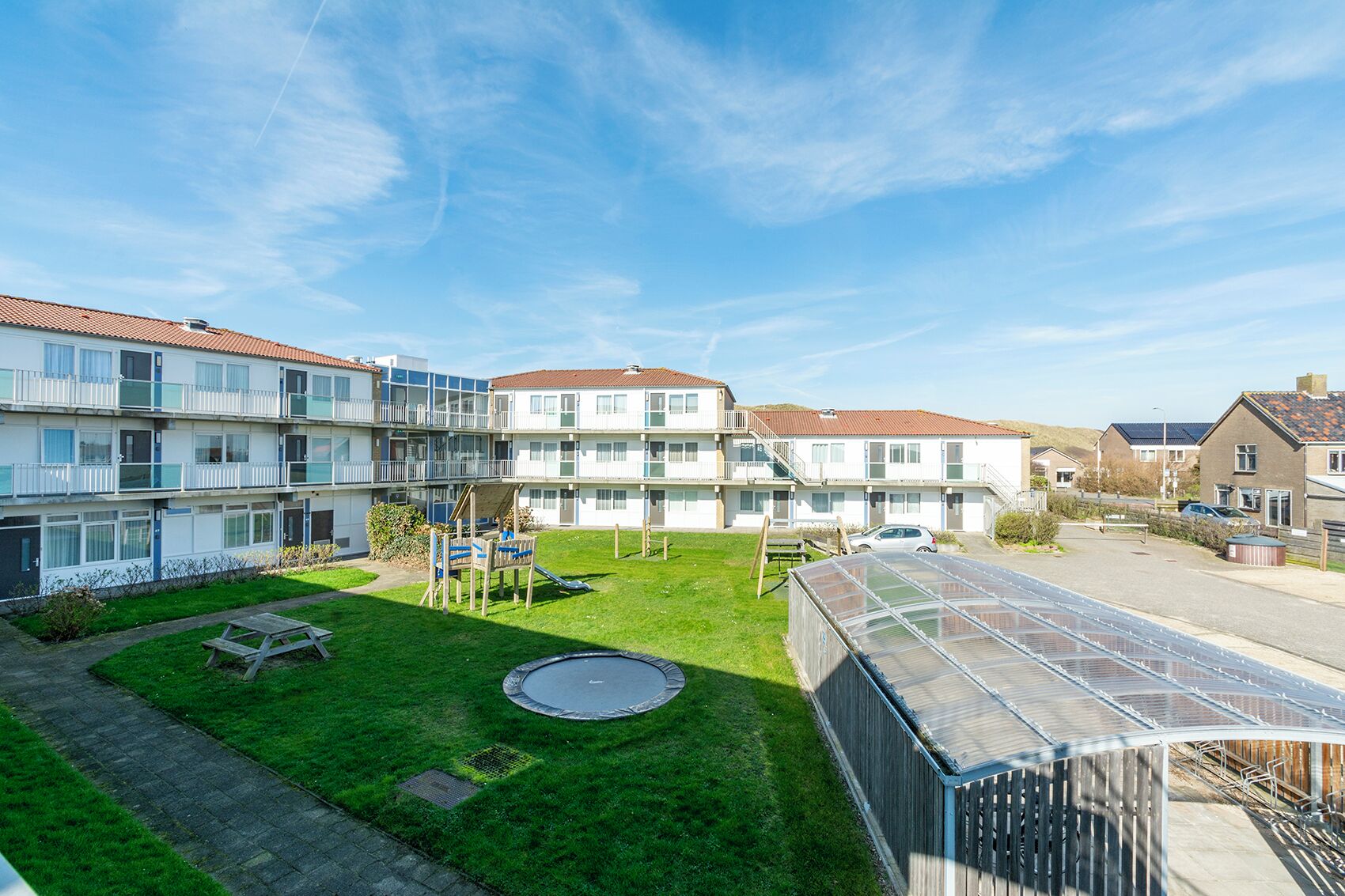 Un immeuble résidentiel doté de nombreux balcons, d’un petit espace verdoyant avec un trampoline et d’une serre.