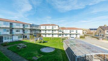 Un immeuble résidentiel doté de nombreux balcons, d’un petit espace verdoyant avec un trampoline et d’une serre.