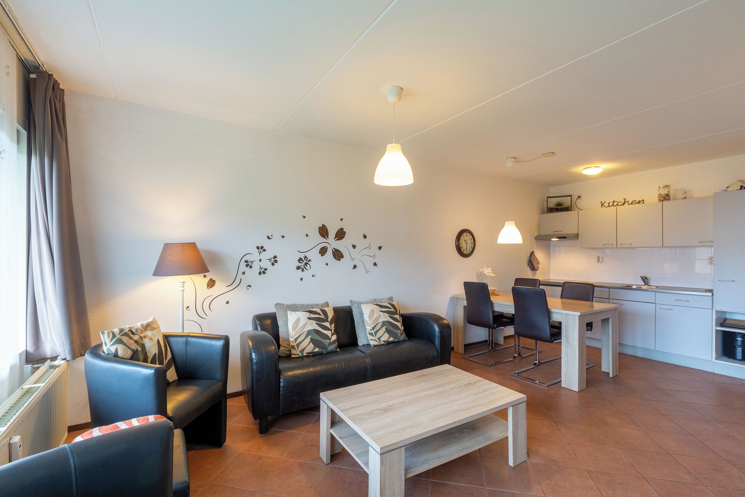 Een moderne woonkamer met een bank, stoelen, een salontafel, en een keuken op de achtergrond.