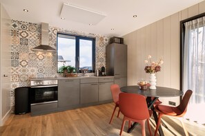 A modern kitchen with a large window, a built-in oven, and a dining area with red chairs. - Zee Vacation Home – Luxury, Peace, and Space on the Coast (Julianadorp)