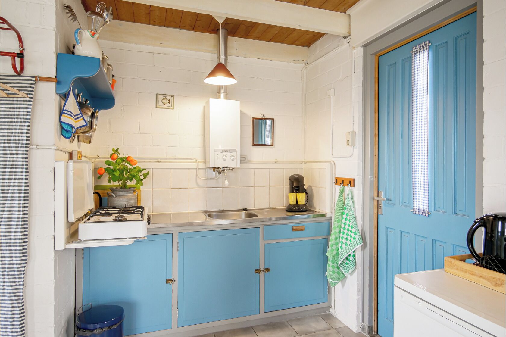 Una cocina con un armario azul, una estufa blanca, un fregadero y una lámpara colgante.