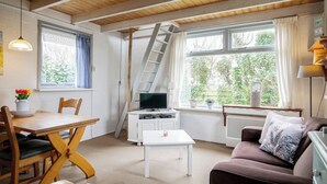 A cozy room with a wooden ceiling, a dining table with chairs, a TV, a sofa, and a window with curtains. - Cozy vacation home for two, close to the beach, the woods, and tulip fields (Callantsoog)