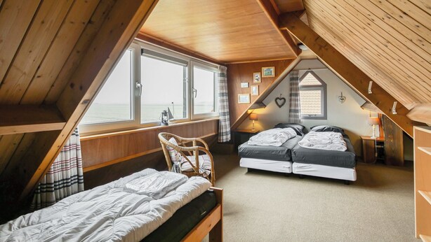 A cozy attic bedroom with a view of the sea, a bunk bed, a single bed, and a small table with a lamp. - Cozy vacation home for two, close to the beach, the woods, and tulip fields (Callantsoog)