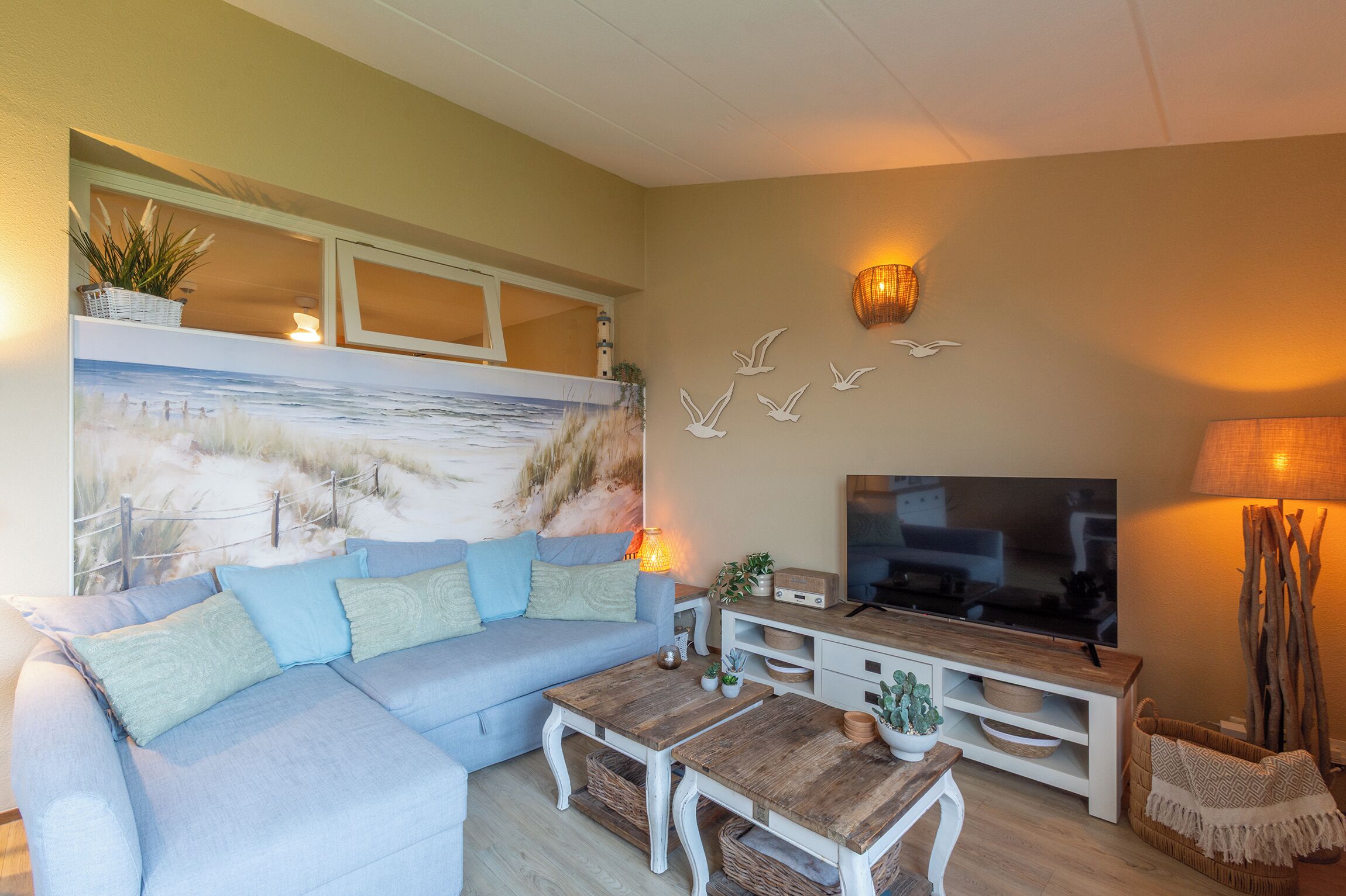 Una sala de estar con sofá, mesa de centro, televisor y decoración en la pared.