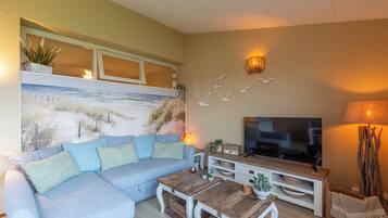 Una sala de estar con sofá, mesa de centro, televisor y decoración en la pared.