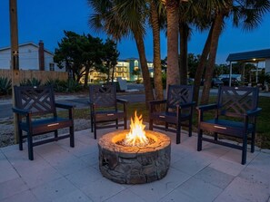 A stone fire pit with chairs around it, set on a tiled patio with palm trees and buildings in the background. - Dolphins Cay - Pet Friendly Condo Center of Town (Cedar Key)