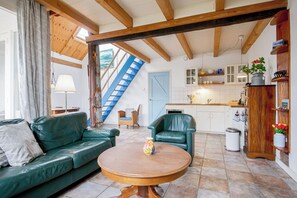 Ein Wohnzimmer mit einem grünen Sofa, einem runden Holztisch, einer blauen Treppe und einer Küche mit weißen Schränken.