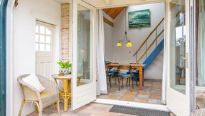 A room with a dining table, chairs, a wicker chair, a small table with a plant, and a staircase. - Cozy vacation rental in a former farmhouse, surrounded by nature. (Callantsoog)