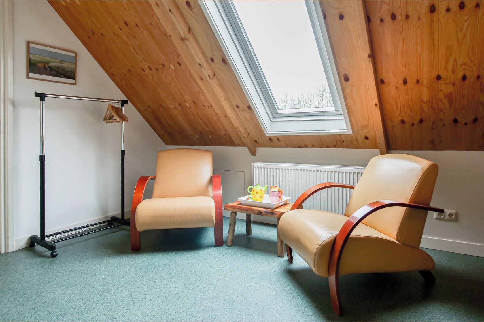 Una stanza con soffitto spiovente, due poltrone in pelle, un tavolino con un vassoio e un termosifone.