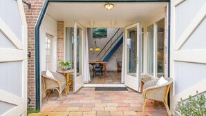 A covered outdoor area with wicker furniture, a dining table, and a staircase leading inside. - Cozy vacation rental in a former farmhouse, surrounded by nature. (Callantsoog)