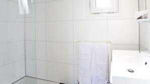 Un baño con azulejos blancos, una cabina de ducha de vidrio, un lavabo blanco y un espejo.
