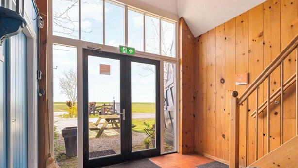 A wooden interior with a staircase, a door leading outside, and a view of the outside. - Spacious studio in an authentic Stolp farmhouse (Schagen)