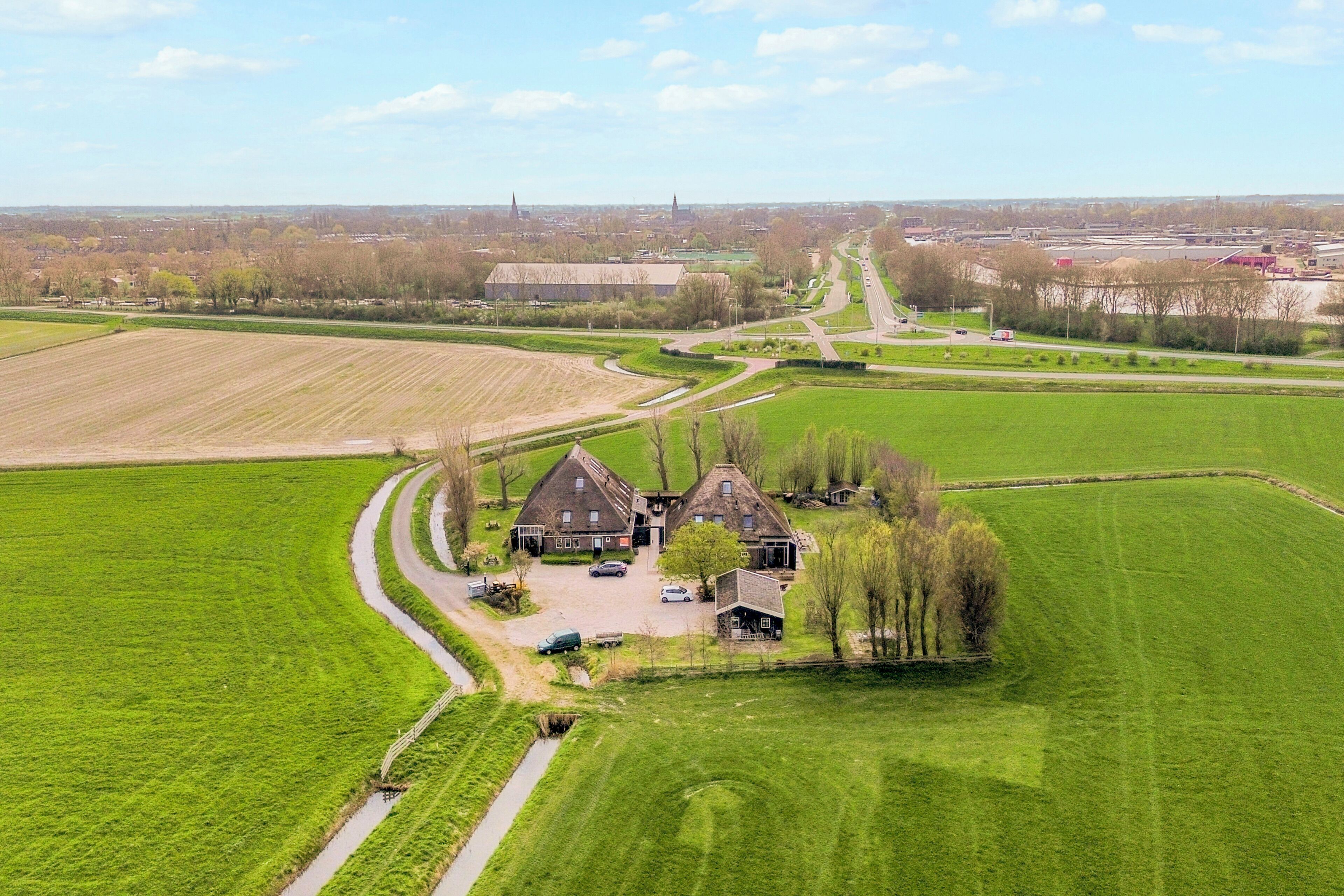 Een landelijk landschap met een groot groen veld, een kronkelende weg en een traditioneel huis met oprit.