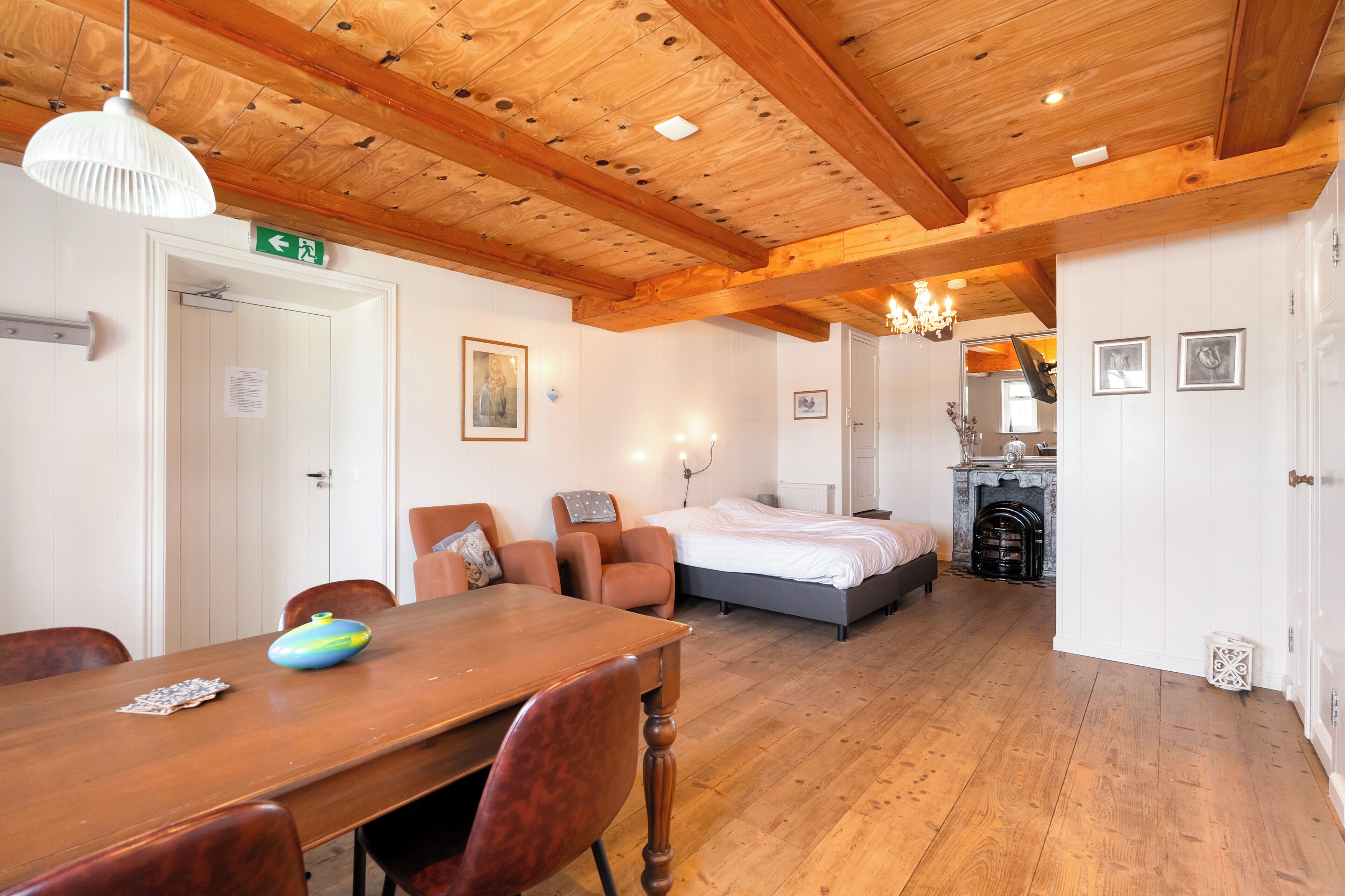 Ein Zimmer mit Holzbalkendecke, einem Bett, einem Esstisch mit Stühlen und einem Kamin.