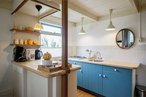 A kitchen with a wooden countertop, blue cabinets, a stove, a sink, and a window with a view of trees. - A cozy stay near the beach, nature, and tulip fields! (Callantsoog)