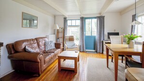En stue med en brun lædersofa, et træsofabord, et spisebord med stole, en lampe og et vindue med gardiner.