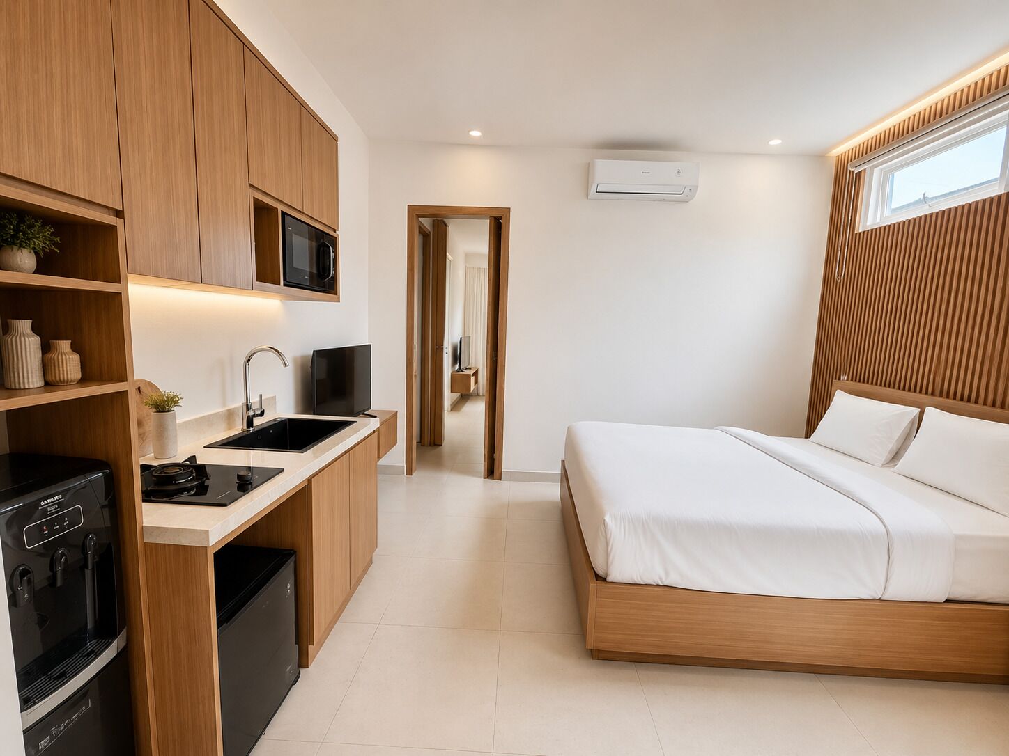 Un dormitorio moderno con una cama de madera, televisión integrada, zona de cocina con microondas y un lavabo.