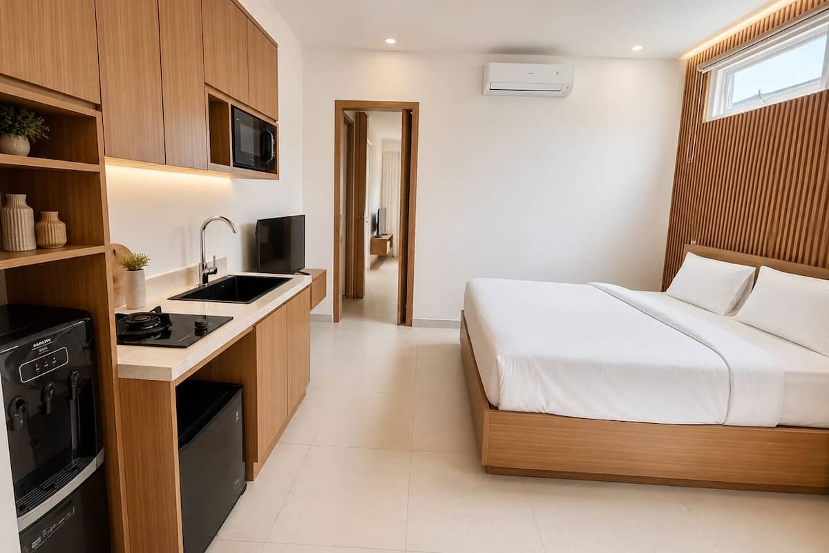 Un dormitorio moderno con una cama de madera, televisión integrada, zona de cocina con microondas y un lavabo.