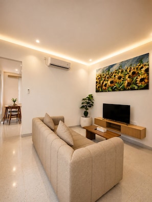 Una sala de estar moderna con un sofá, un televisor de pantalla plana, una mesa de centro y un cuadro de girasoles.