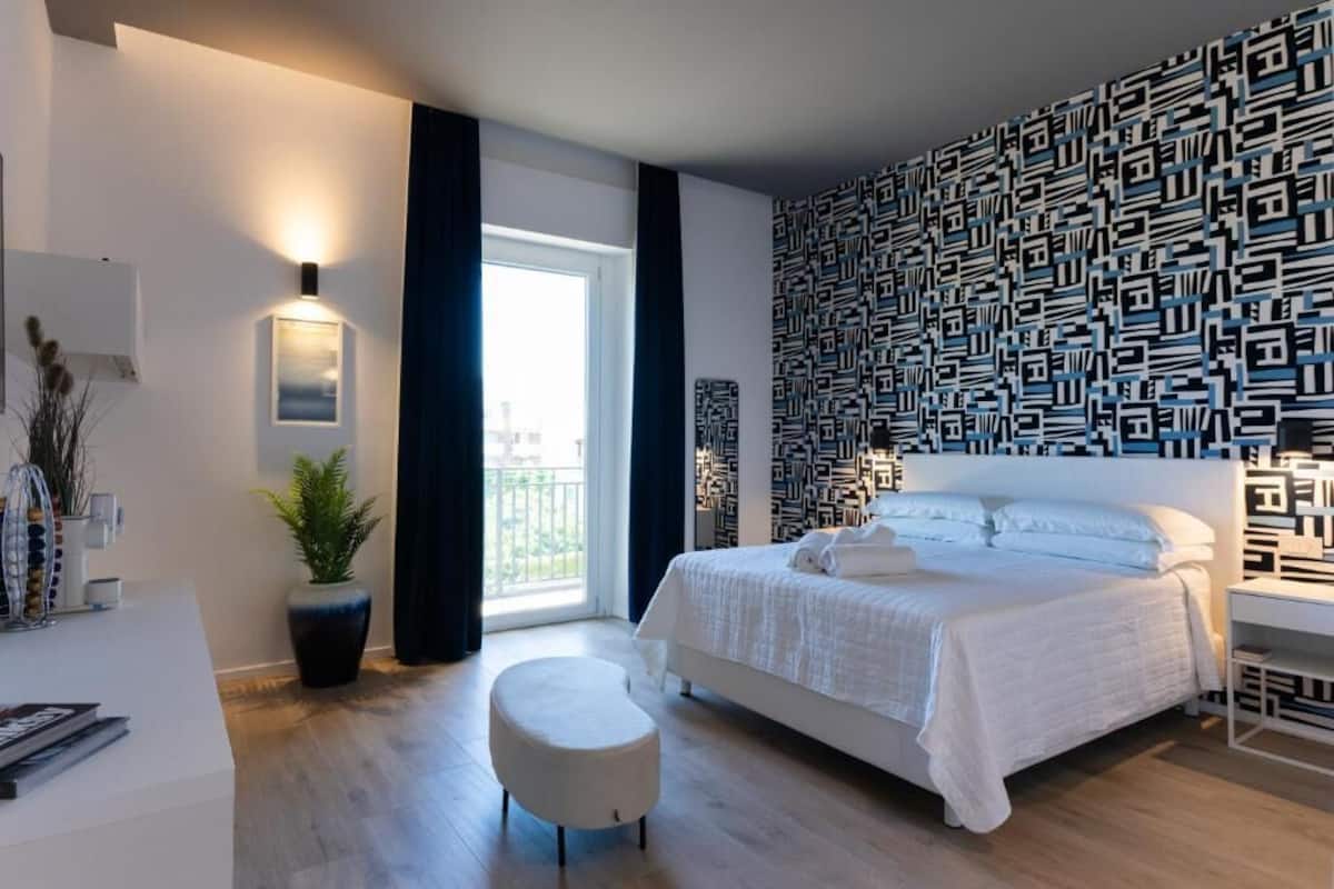 Un dormitorio moderno con una cama grande, una planta en maceta, un banco blanco y una pared con estampado.