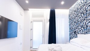 A modern hotel room with a bed, a flat-screen TV, a door leading to a balcony, and a patterned wall.