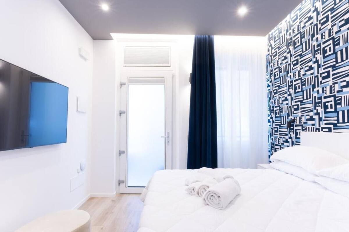 Habitación de hotel moderna con cama, televisión de pantalla plana, puerta que da a un balcón y pared con estampado.