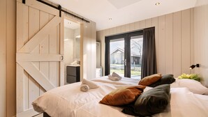 Ein Schlafzimmer mit einem großen Bett, einer Schiebetür im Scheunenstil, einem Fenster mit Ausblick und einem Nachttisch mit Lampe.
