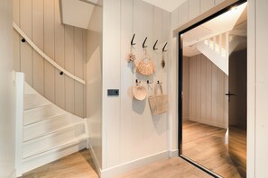 A staircase with a wooden finish, a wall-mounted hook with a woven bag, and a door leading to another room. - Luxury & Relaxation at the Zee & Zand Family House<br> <br>Welcome to the Zee & Zand Family House—your brand-new vacation home, where luxury, comfort, and flexibility come together perfectly.<br>The accommodation consists of two beautiful 4-person— (Julianadorp)