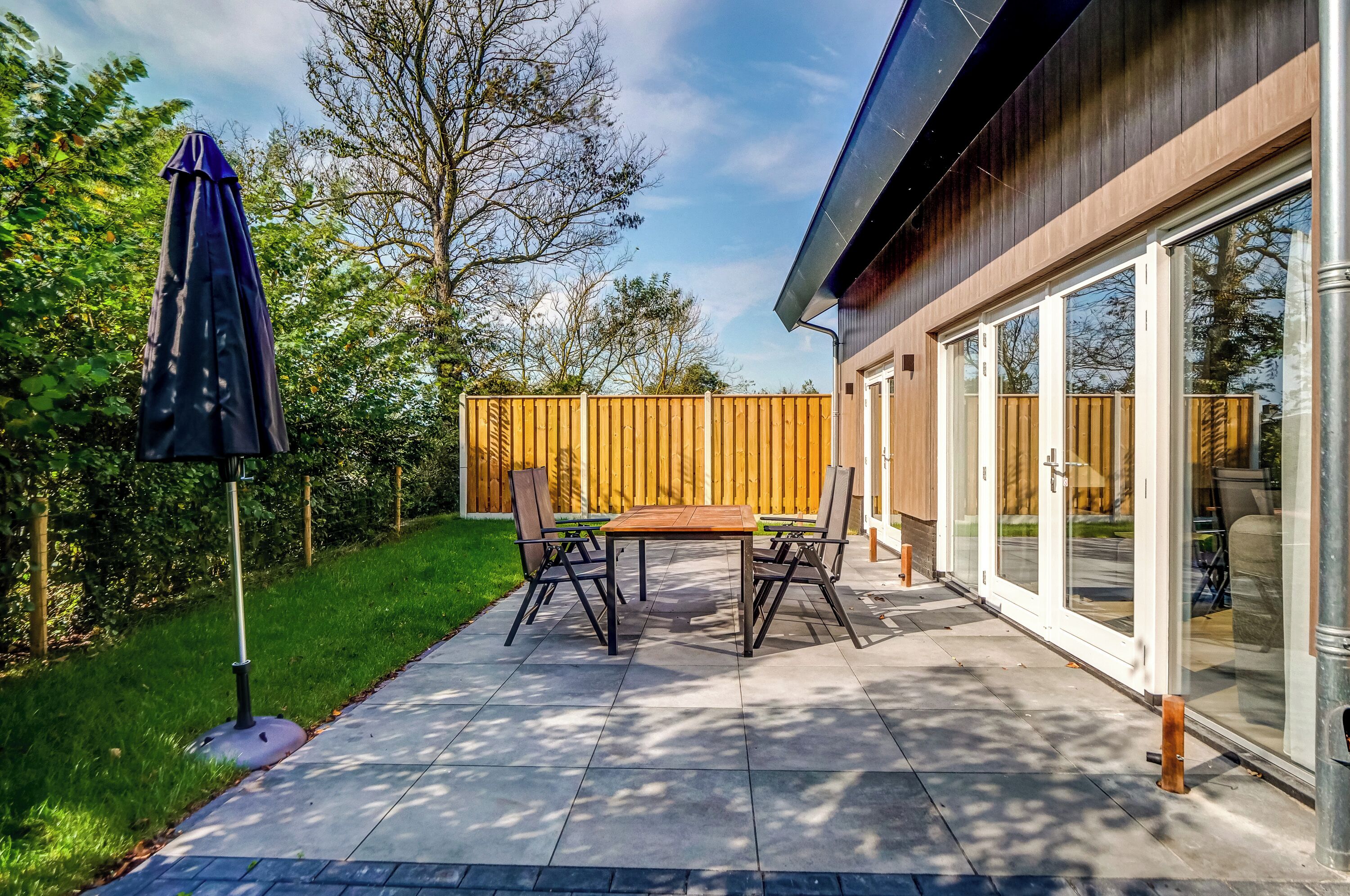 An outdoor patio with a table and chairs, a covered umbrella, and a wooden fence.