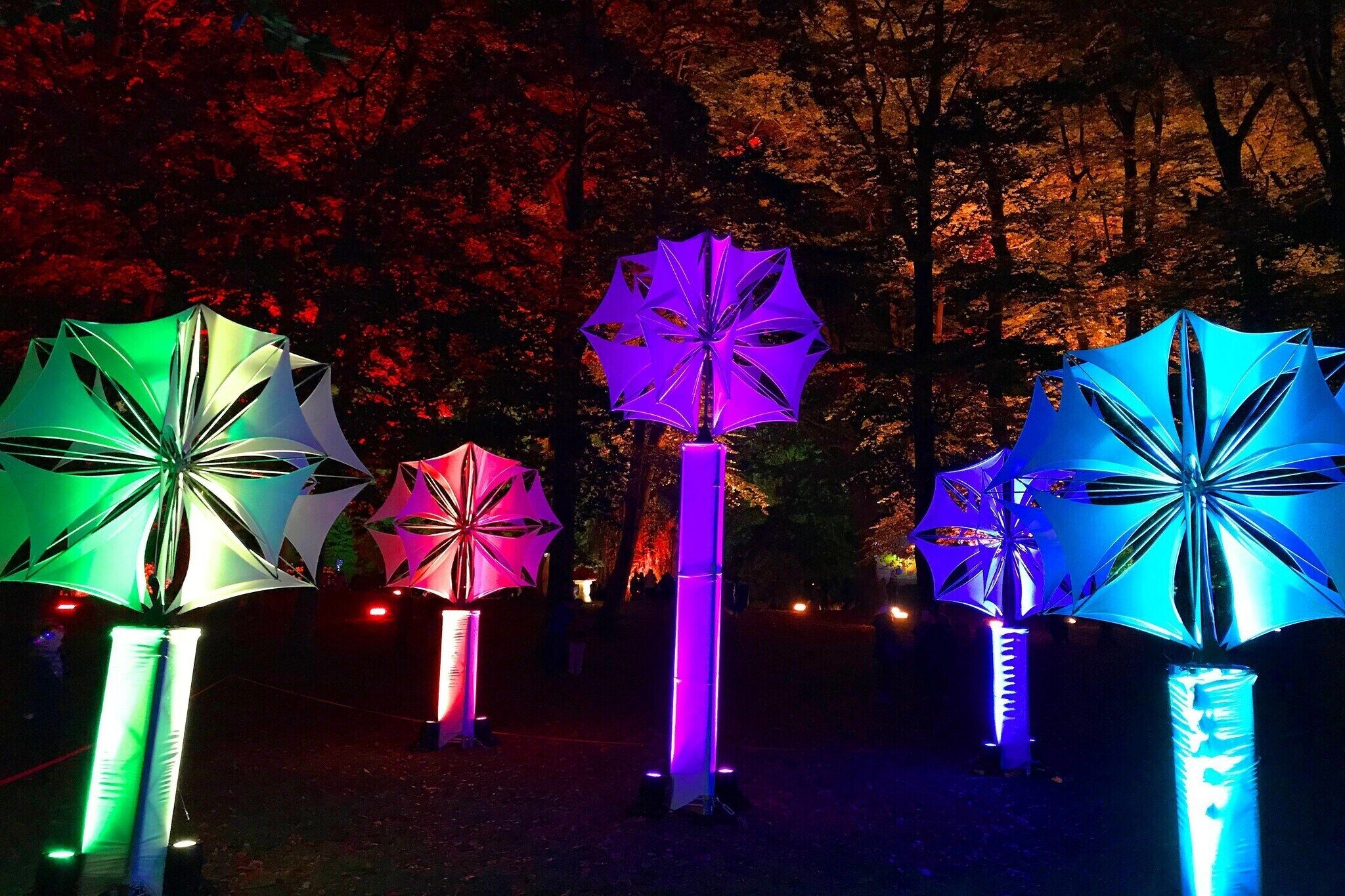 Tres esculturas de sombrillas iluminadas en un espacio al aire libre.